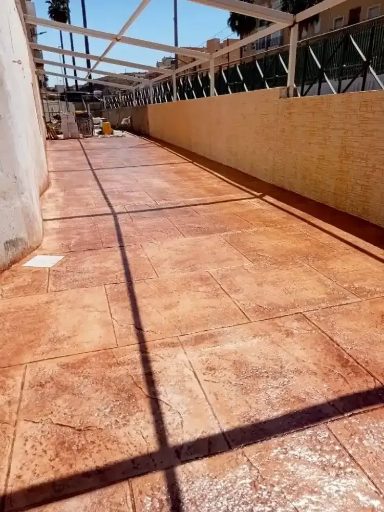 Patio de hormigón estampado con toldo blanco y pared color canela.
