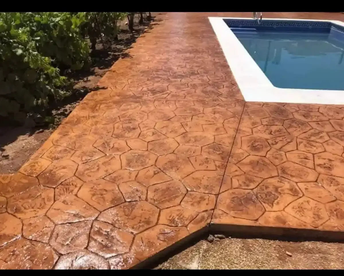 Patio de hormigón estampado con piscina al fondo, que presenta un patrón similar a la piedra en tonos marrones.