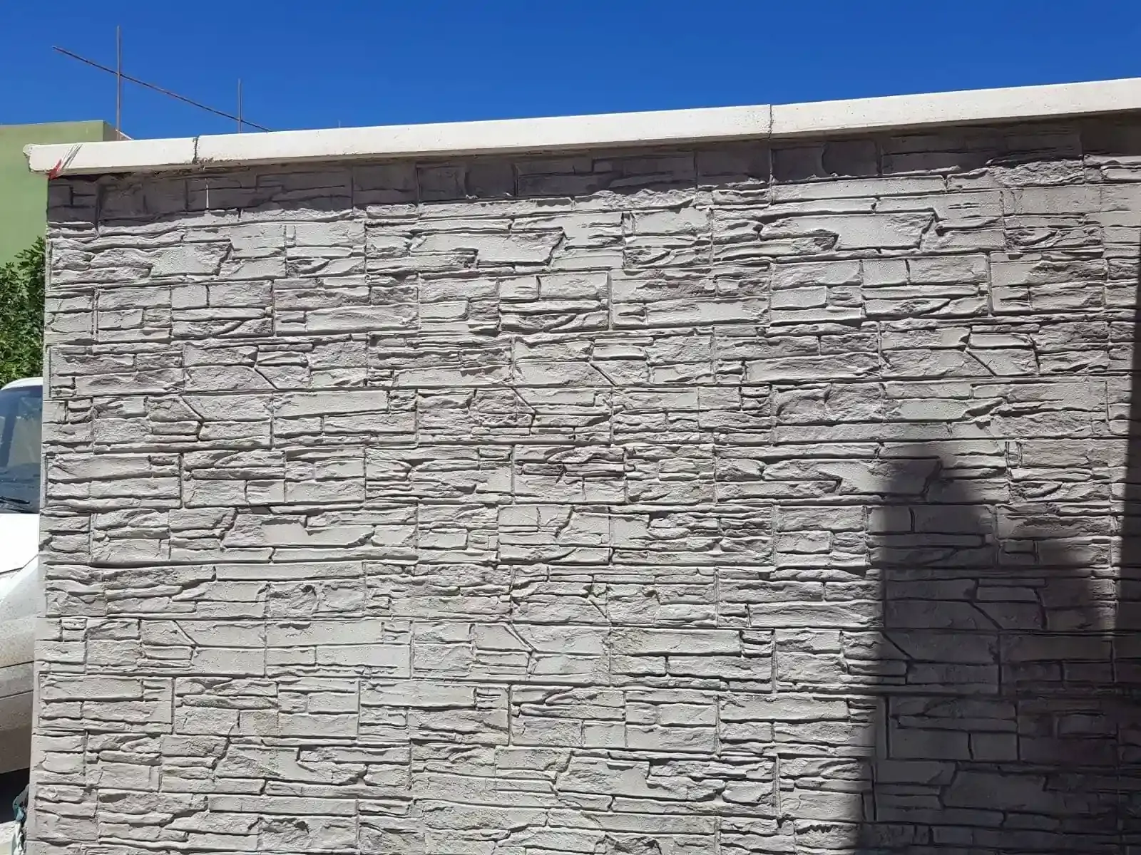 Muro de ladrillo de piedra gris con la parte superior blanca bajo un cielo azul.