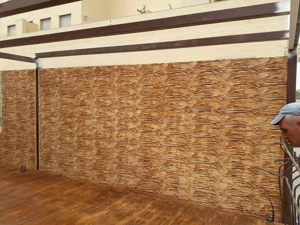 Espacio exterior con paredes de madera y vigas marrones. Una persona mira hacia la pared.