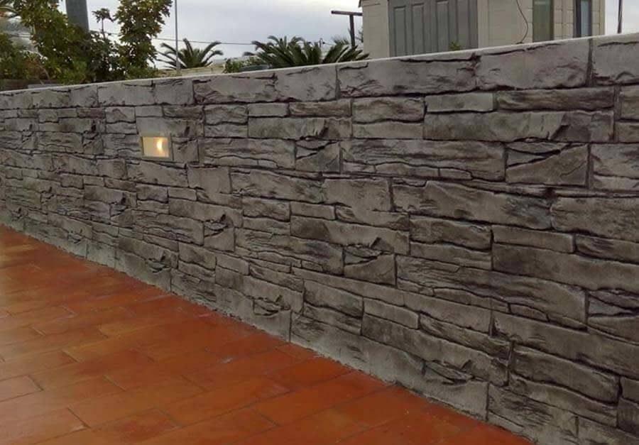 Pared gris con textura de piedra y luz incorporada, junto a un patio color terracota.
