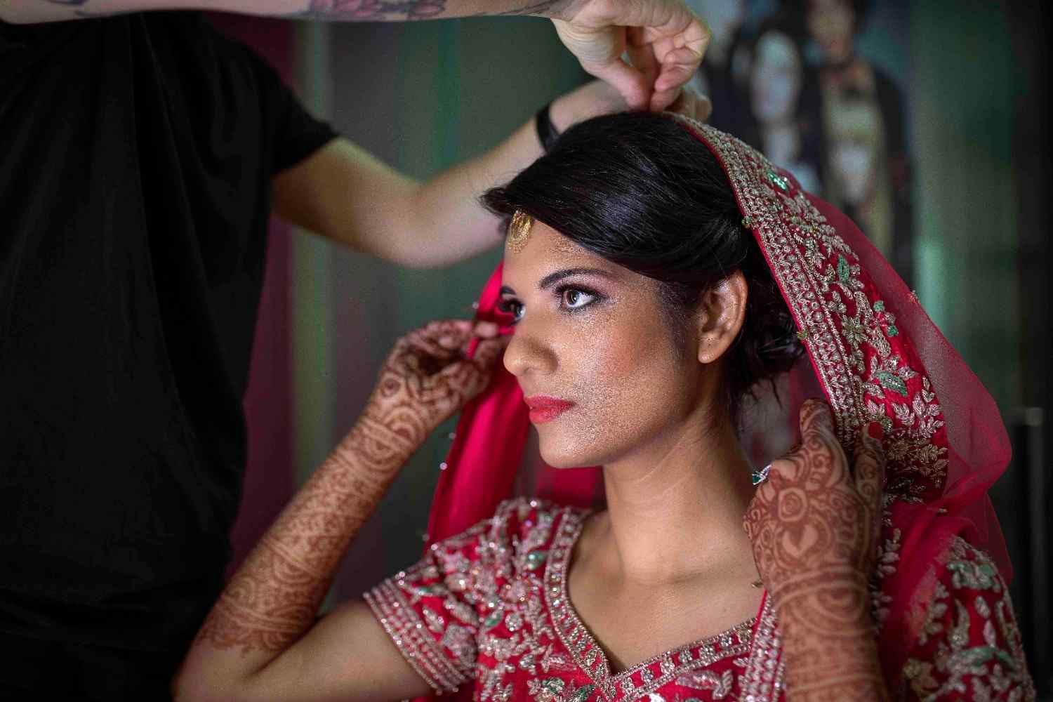 La novia se está ajustando el velo rojo y la henna durante los preparativos de la boda.