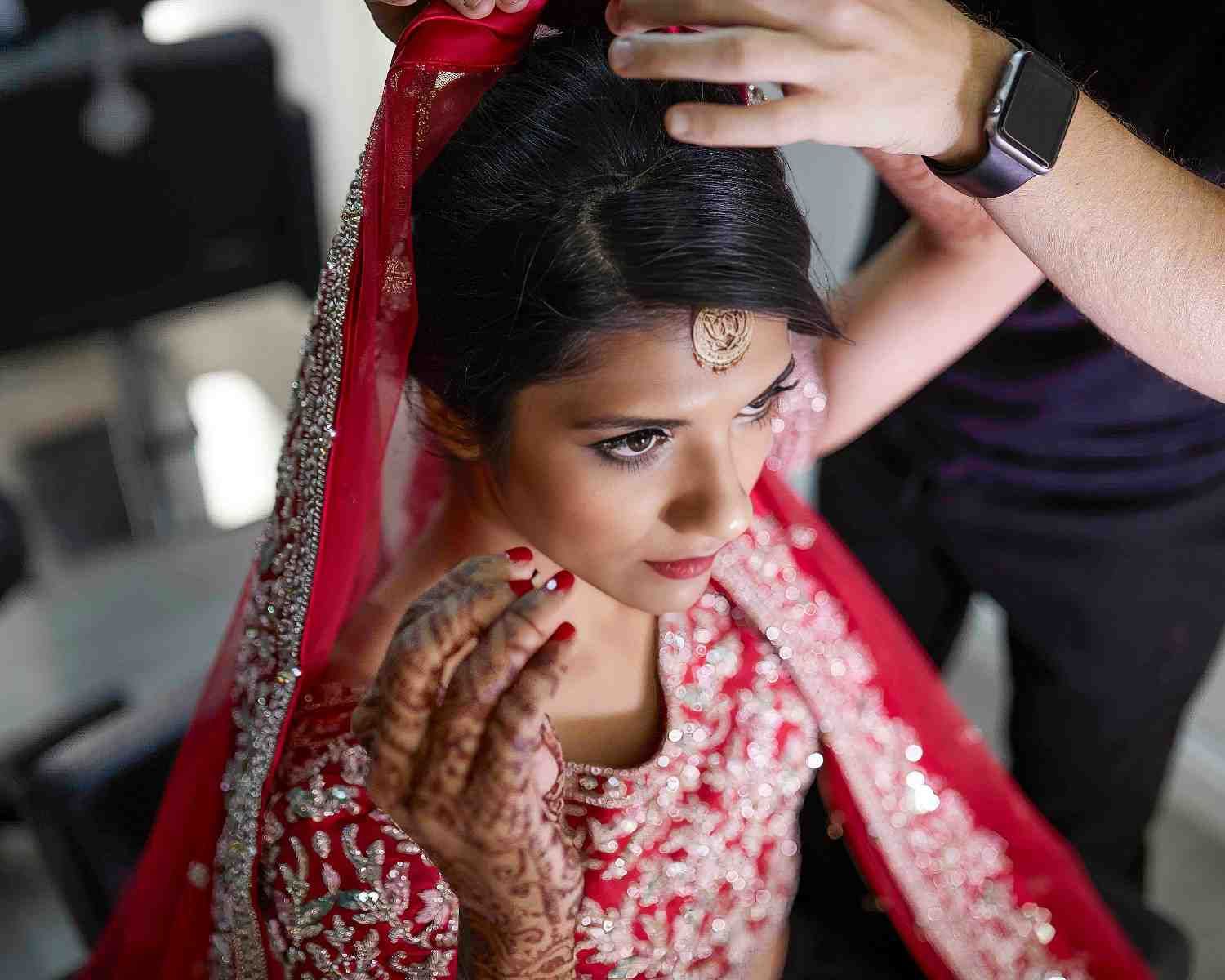 Novia con traje nupcial rojo a la que le están ajustando el tocado, con henna en la mano y el brazo.