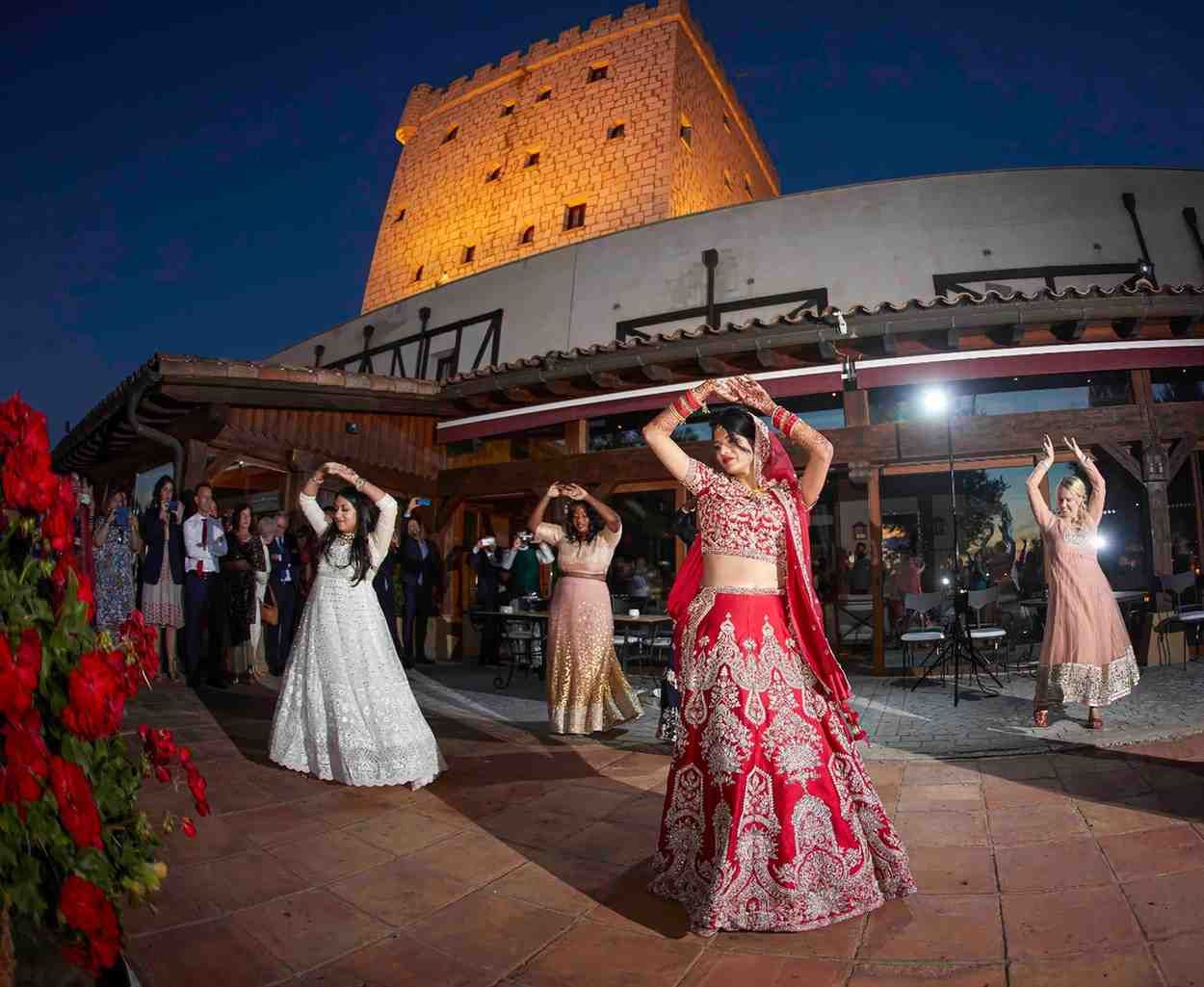Bailarines con coloridos vestidos actúan al aire libre por la noche frente a una torre histórica iluminada.