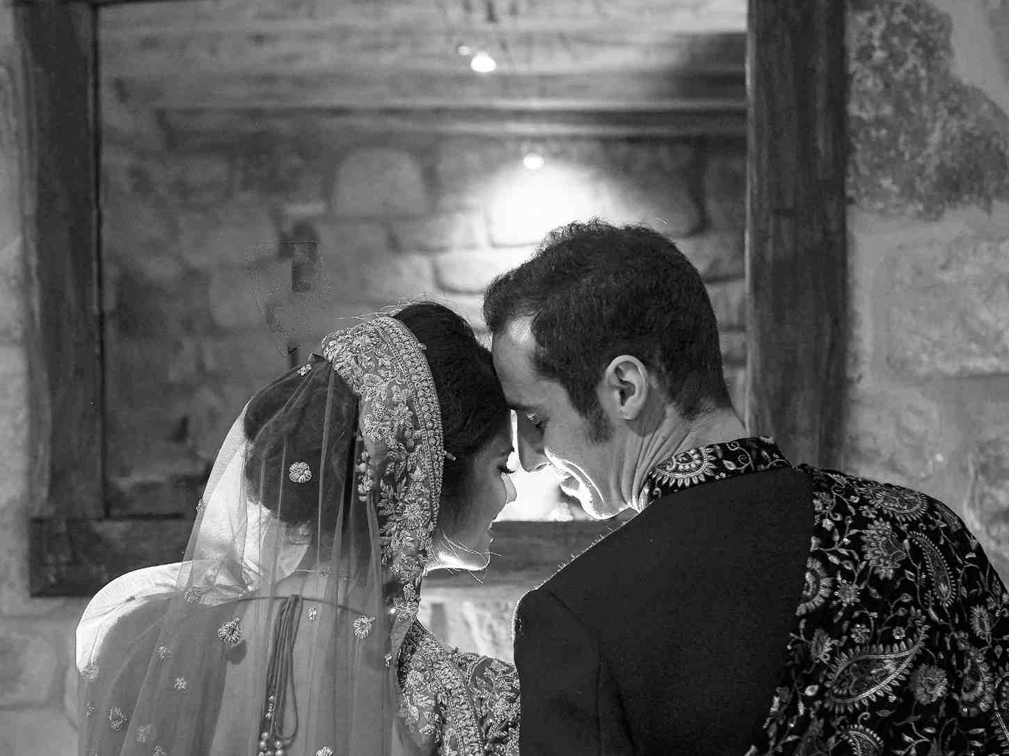 Una pareja vestida de gala se apoya la una en la otra junto a un altar iluminado con velas en una habitación de piedra.