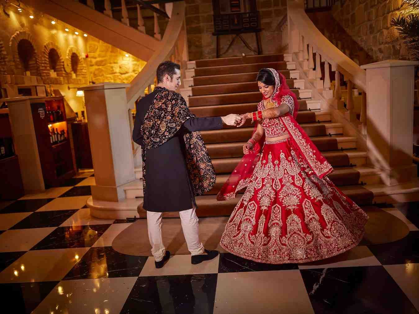Una pareja con elaborados trajes tradicionales baila en una gran escalera en un salón cálidamente iluminado.