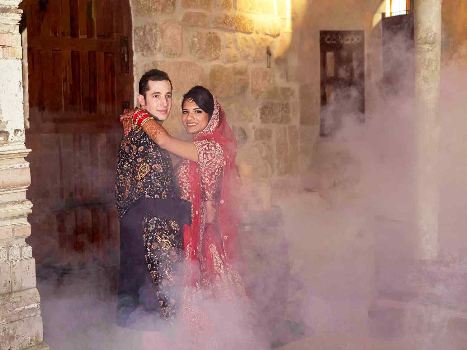 Una pareja vestida de etiqueta se abraza entre el humo en una habitación de piedra.