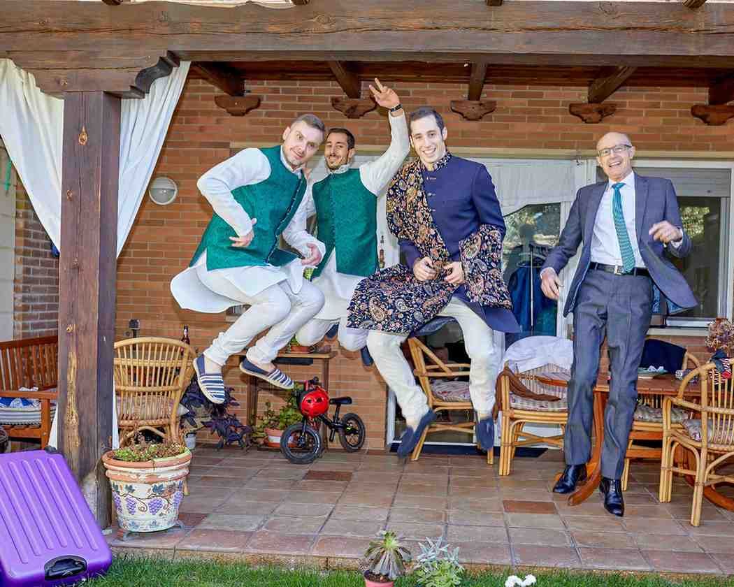 Cuatro personas con atuendos festivos posan en pleno salto en un patio de madera con sillas y decoración rústica.