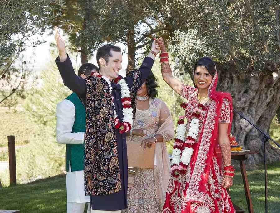 Dos personas con elaborados trajes tradicionales se toman de las manos durante una ceremonia de boda al aire libre.