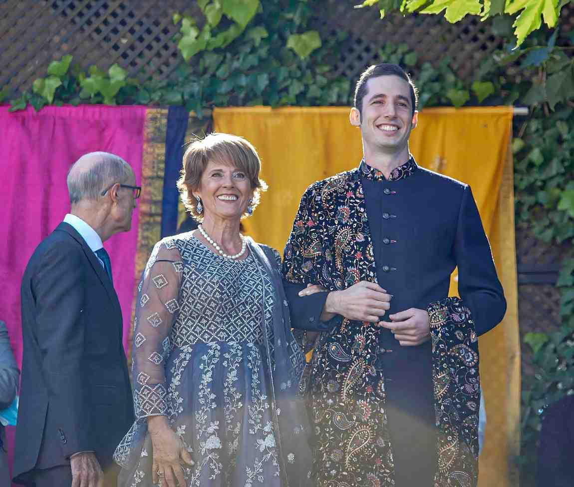Tres personas en un escenario con cortinas de arcoíris y amarillas, sonriendo y vestidas con atuendo formal.