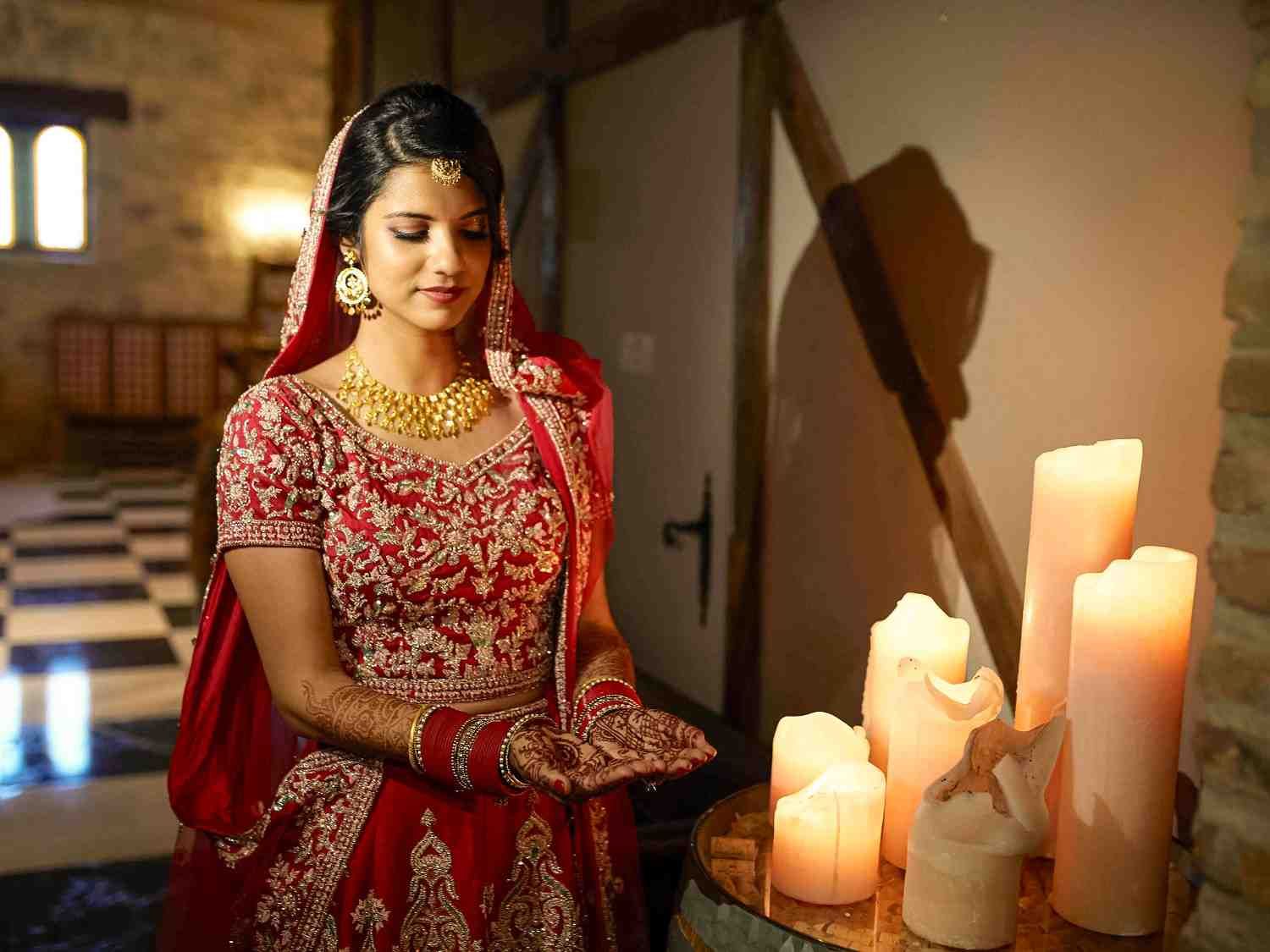 Mujer con vestido rojo de pie junto a velas encendidas en una habitación cálida y rústica.