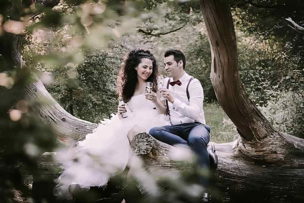 Una pareja sentada en la rama de un árbol en un parque frondoso, sonriendo y conversando entre un follaje suave y difuminado.