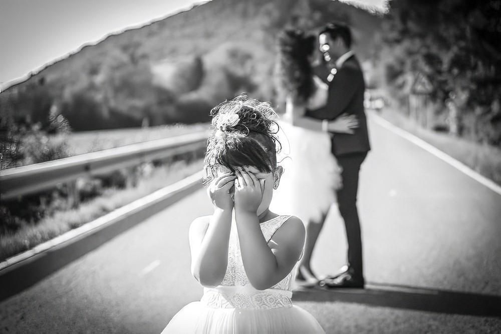 La novia se cubre el rostro en la carretera mientras el novio permanece desenfocado al fondo.