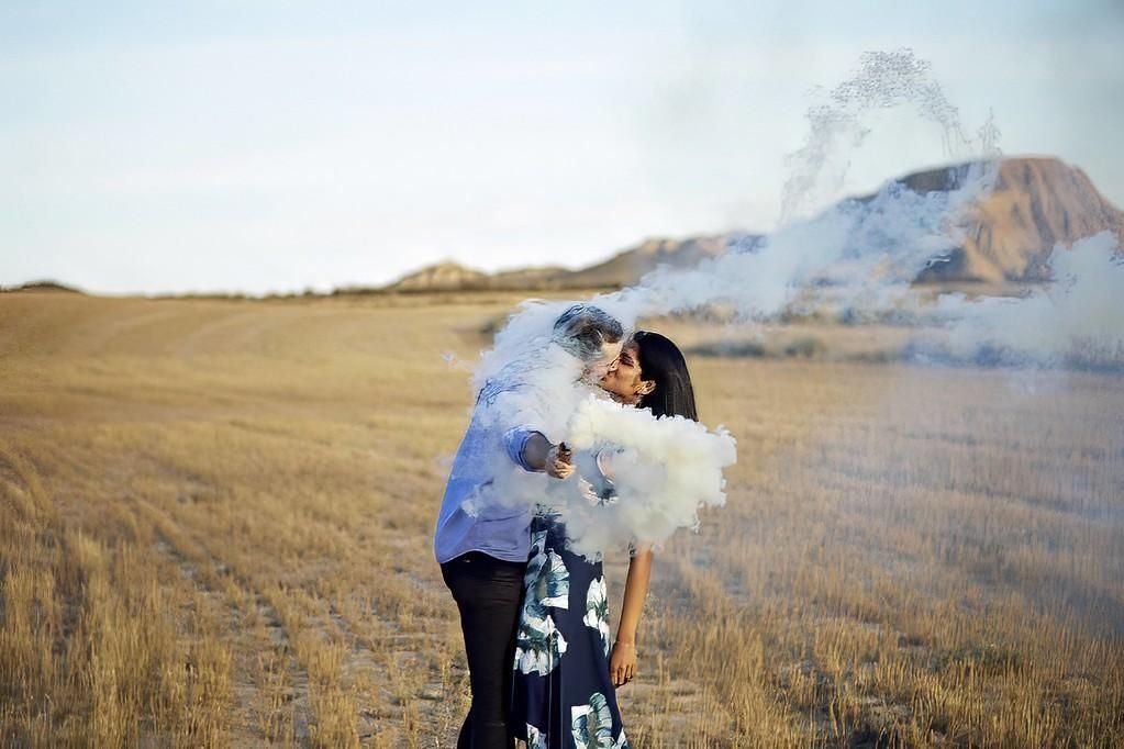 Una pareja se abraza en un campo dorado mientras una nube de humo azul los envuelve.