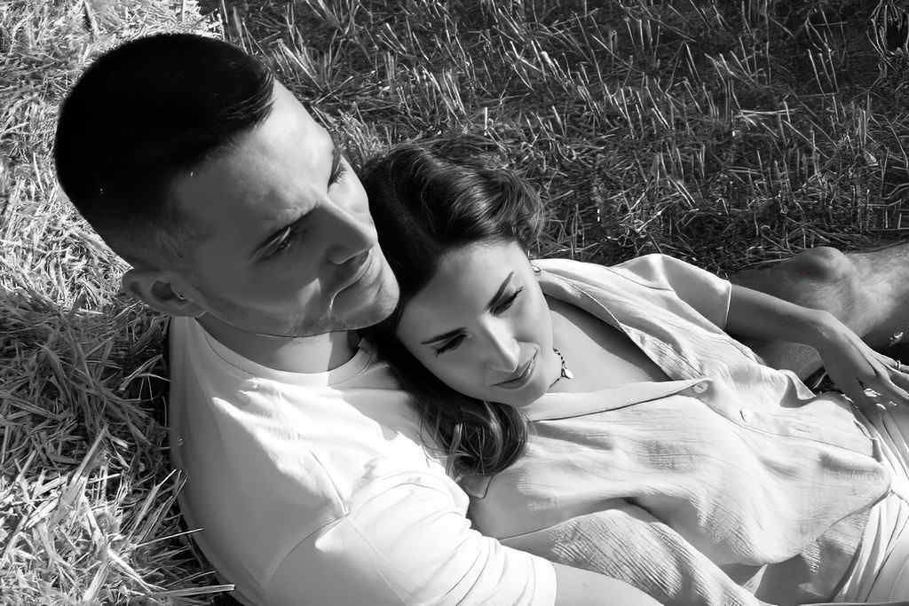 Pareja tumbada en la hierba, apoyada la una en la otra en una fotografía en blanco y negro.