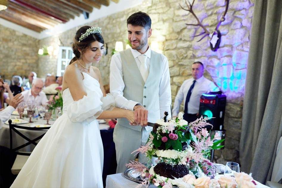 Los novios cortan un pastel de bodas cubierto de flores en una recepción.