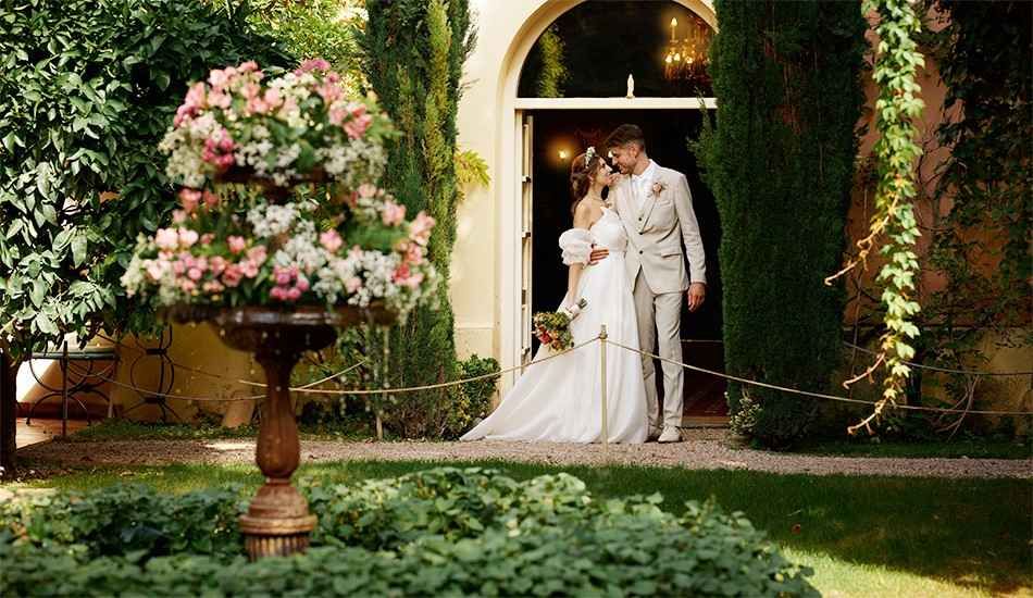 Los novios se besan bajo un arco floral en una exuberante escena de boda en un jardín.