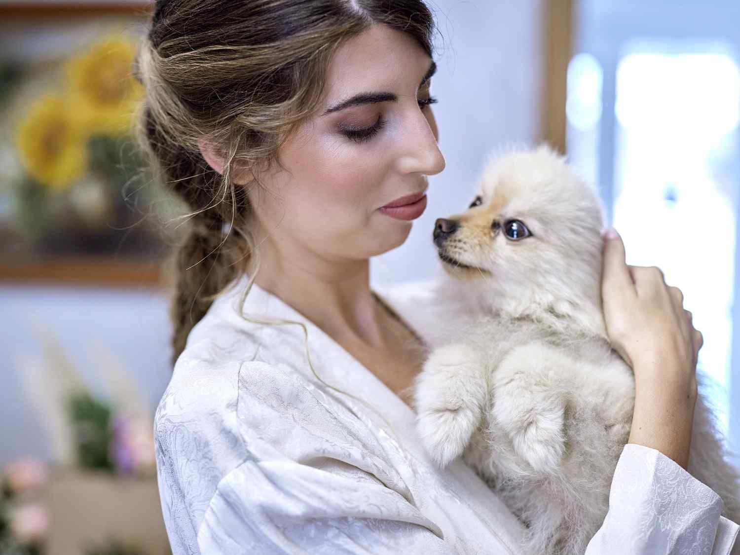 Mujer con bata blanca sosteniendo un cachorro esponjoso de color crema y mirándolo con cariño.