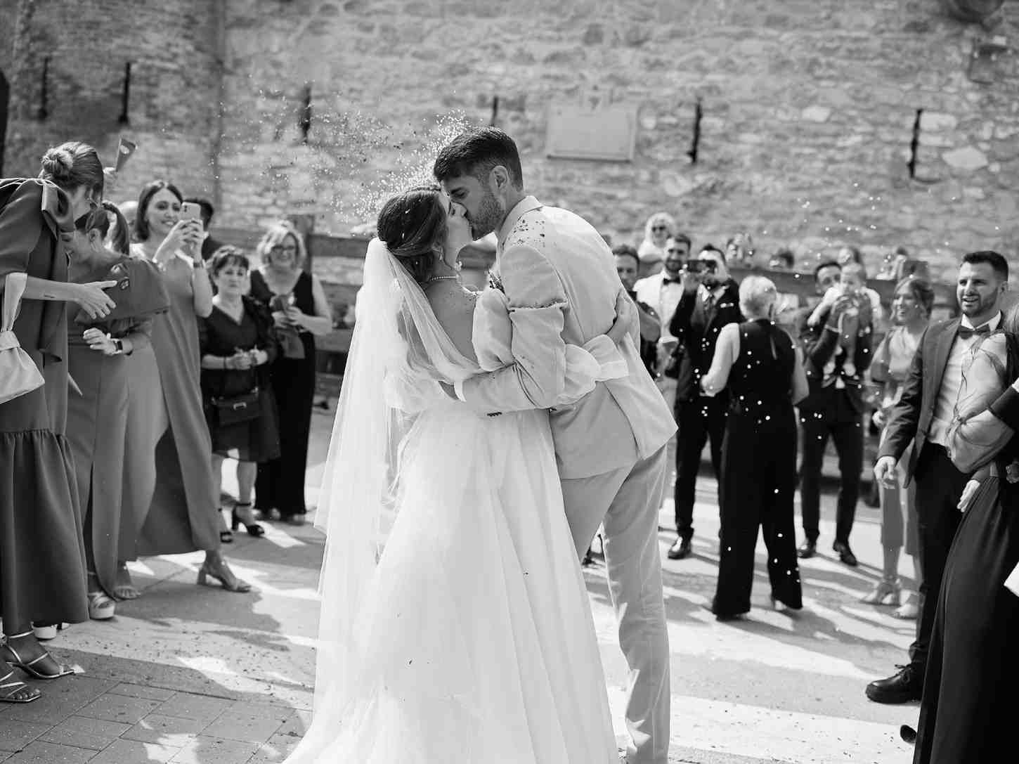 Los novios se abrazan durante una ceremonia nupcial al aire libre mientras los invitados aplauden cerca.