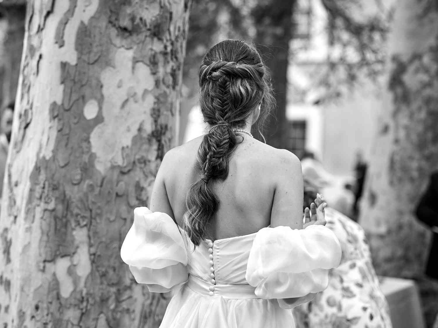 Mujer con vestido blanco vista de espaldas entre troncos de árboles en un entorno boscoso.