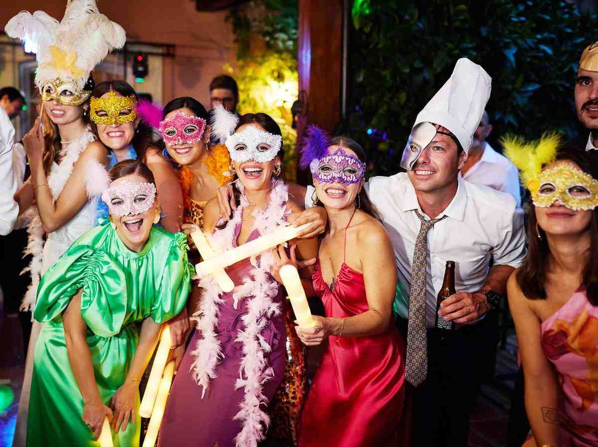 Grupo de personas con coloridas máscaras y disfraces celebrando una animada fiesta en el interior.