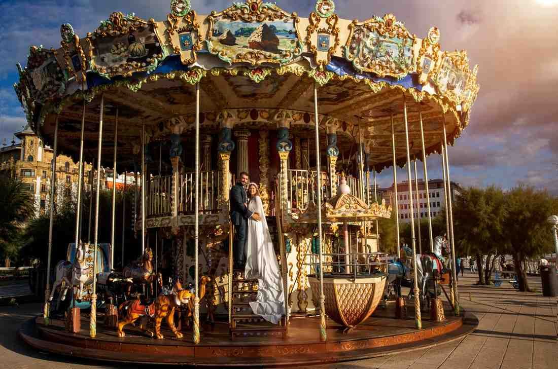 Un carrusel ornamentado con detalles dorados y caballos blancos en un paseo marítimo al atardecer.