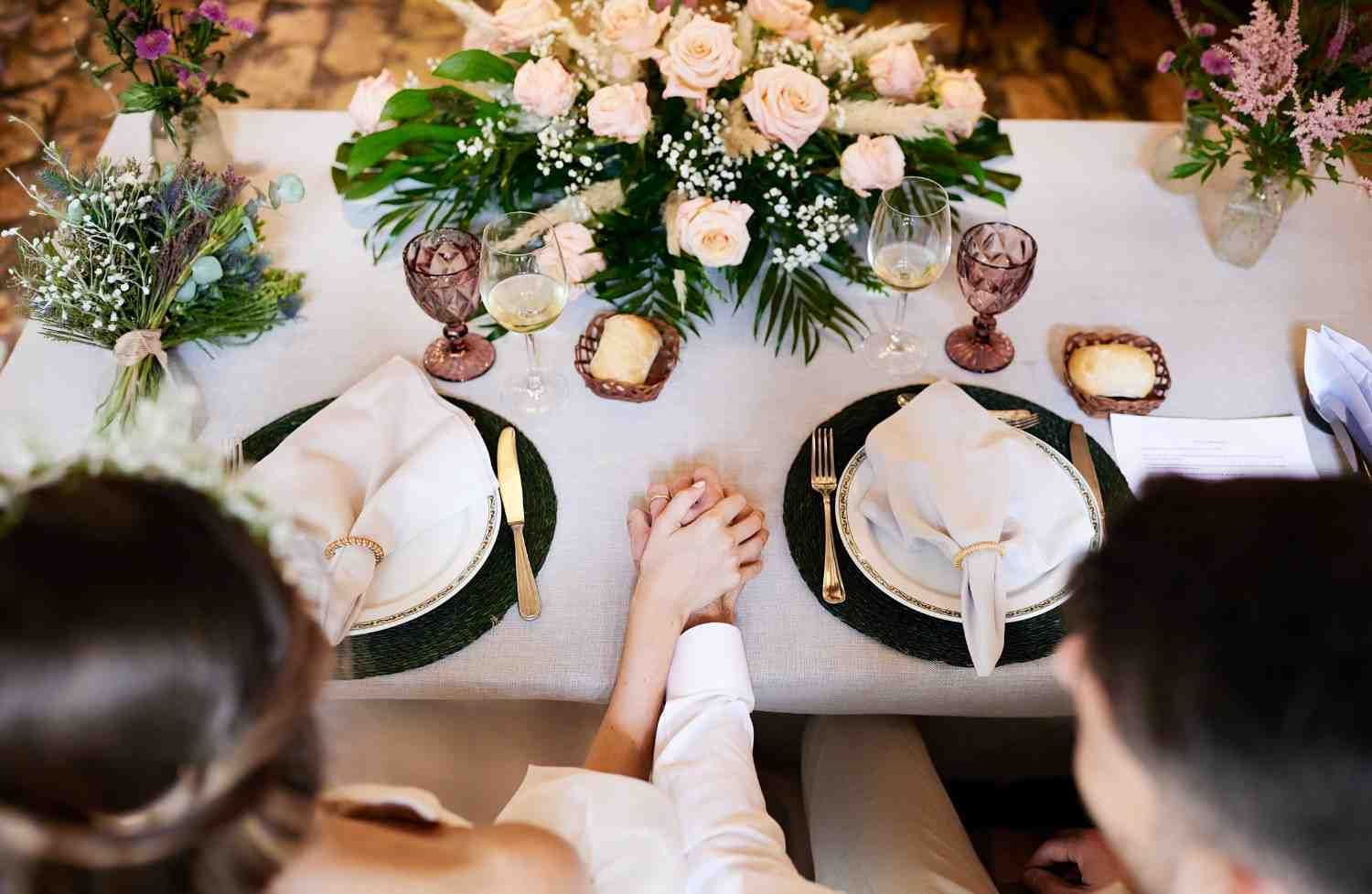 Vista desde arriba de una mesa de cena iluminada con velas, con centros de mesa florales y dos personas.