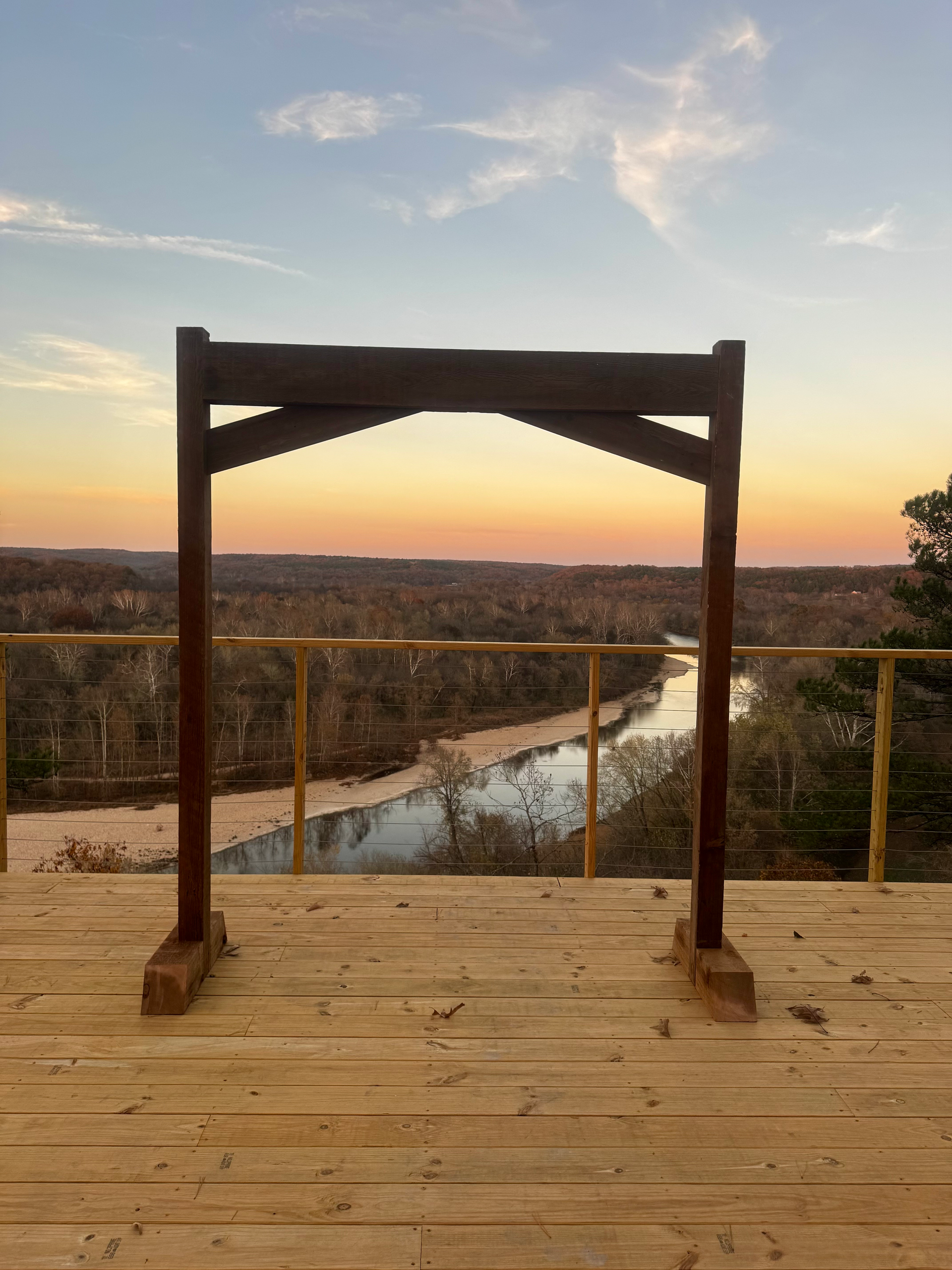 Wooden arch on a deck overlooking a river and sunset.