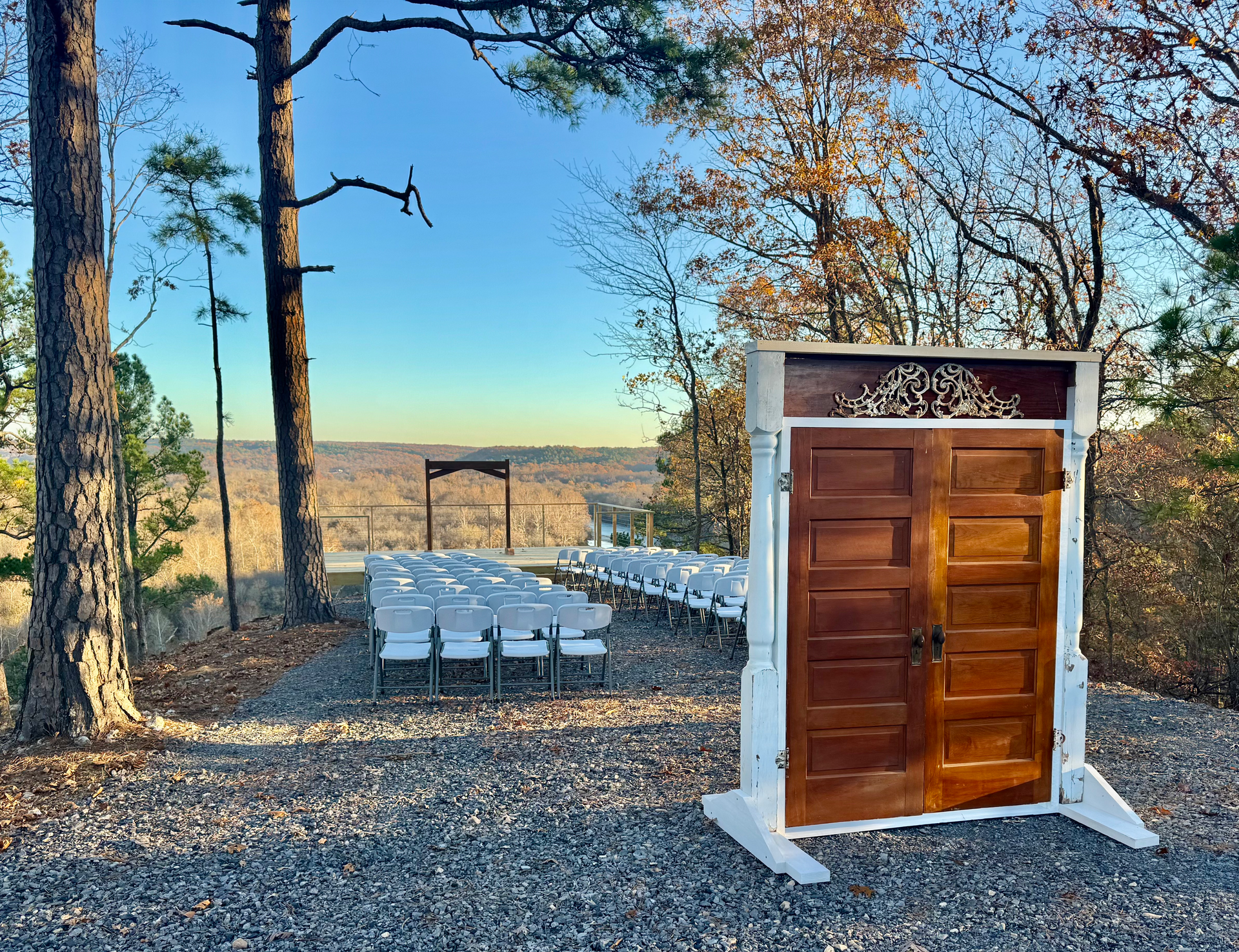 Wedding ceremony setup with wooden doors, chairs, and arbor overlooking a vista.