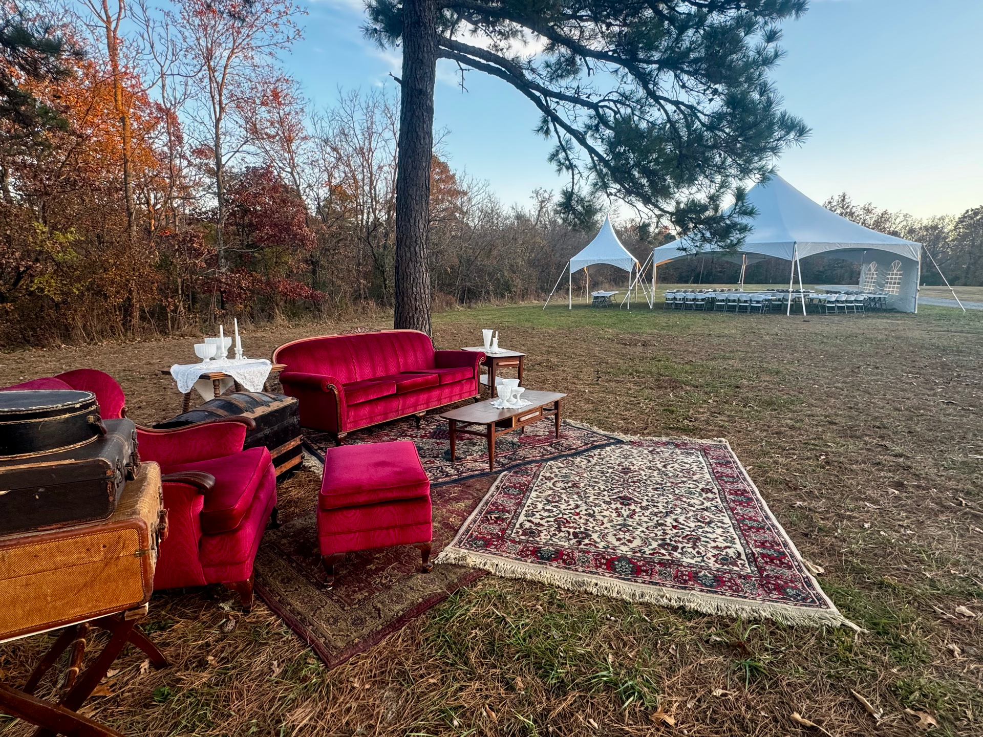 Outdoor lounge area with red velvet furniture and rugs, with a white tent in the background.
