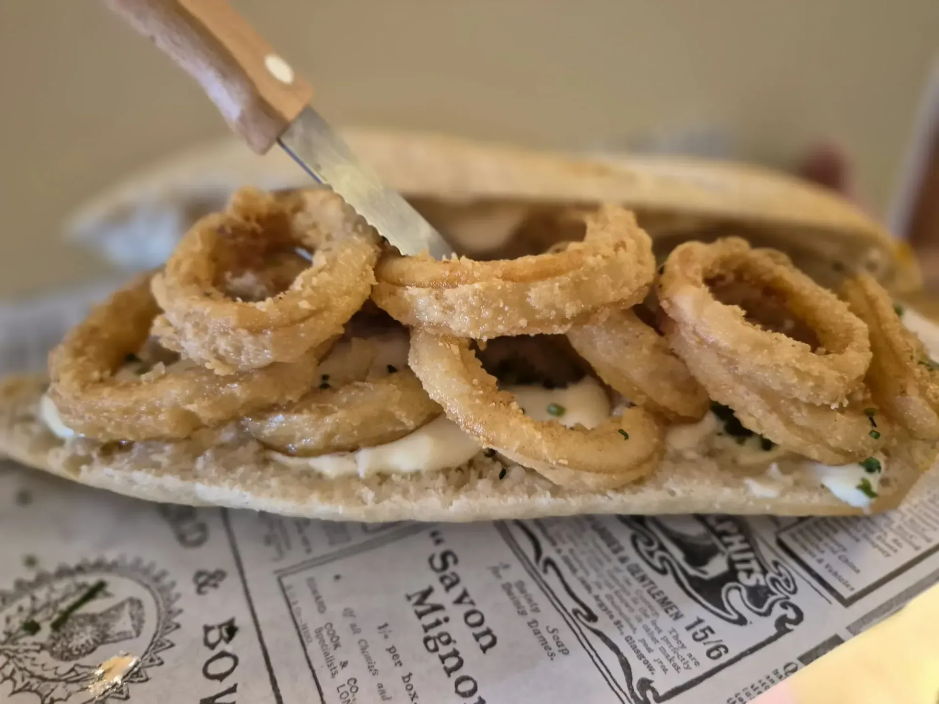 Sándwich con aros de cebolla fritos, cortados con cuchillo, sobre un papel de periódico.
