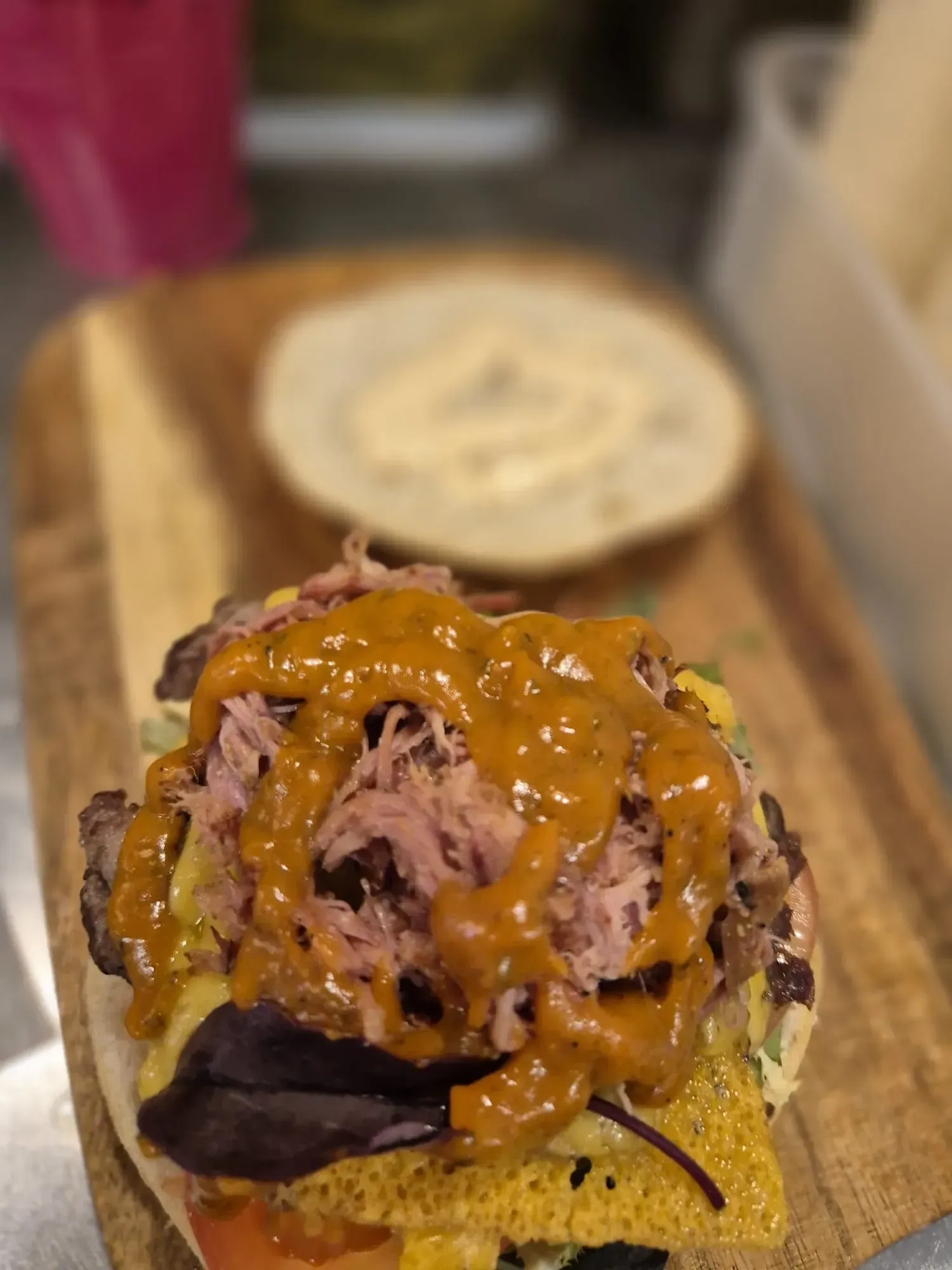 Hamburguesa sobre tabla de madera con cerdo desmenuzado, salsa y un pan con mayonesa encima.