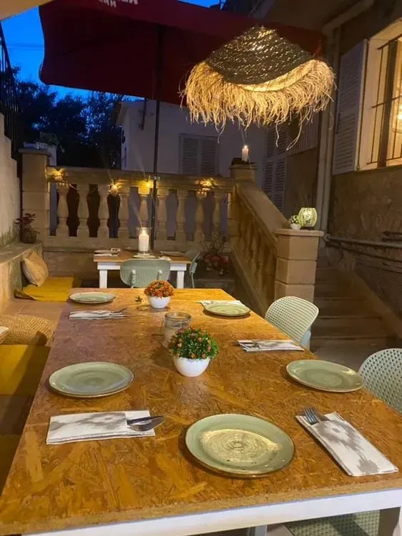 Mesa de comedor al aire libre para invitados bajo una lámpara de paja y una sombrilla roja.