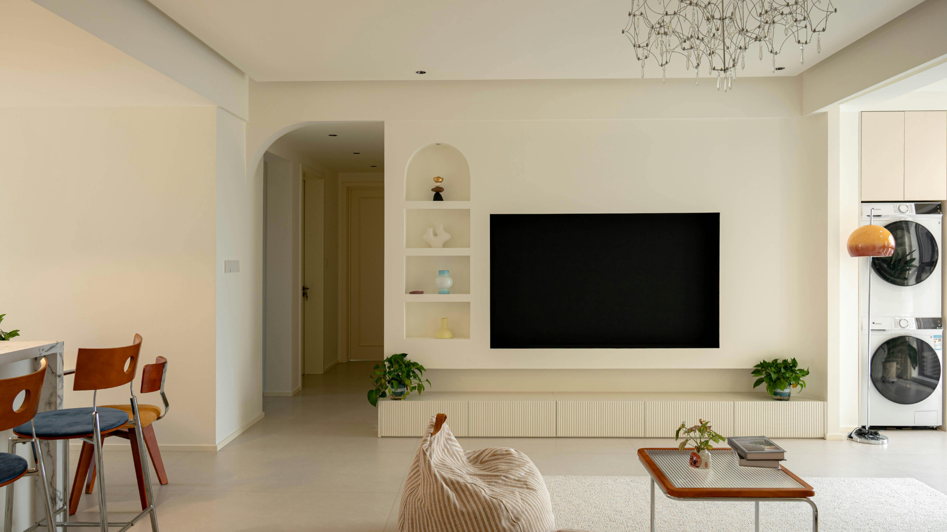 Salon avec murs couleur crème, télévision, étagères intégrées et laveuse/sécheuse superposées.