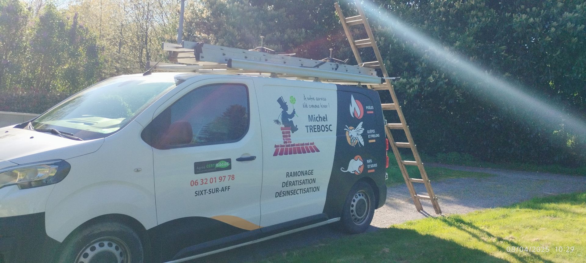Fourgonnette de service blanche avec une échelle appuyée contre elle sur une pelouse avec des arbres en arrière-plan.