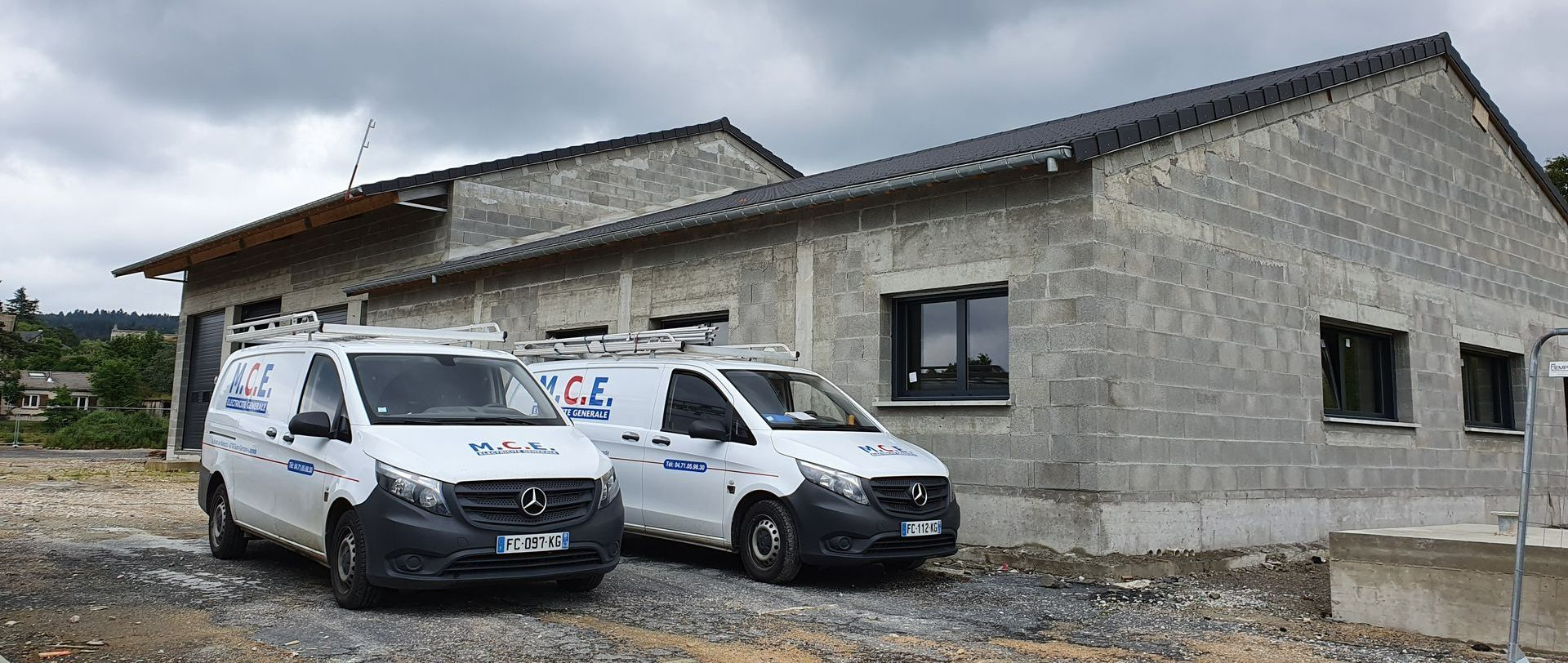 Deux camions blancs de l'entreprise M.C.E devant une maison en construction