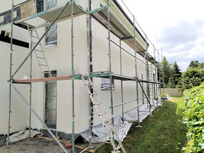 Des échafaudages entourent une maison en cours de peinture beige clair, avec des bâches en plastique au sol.