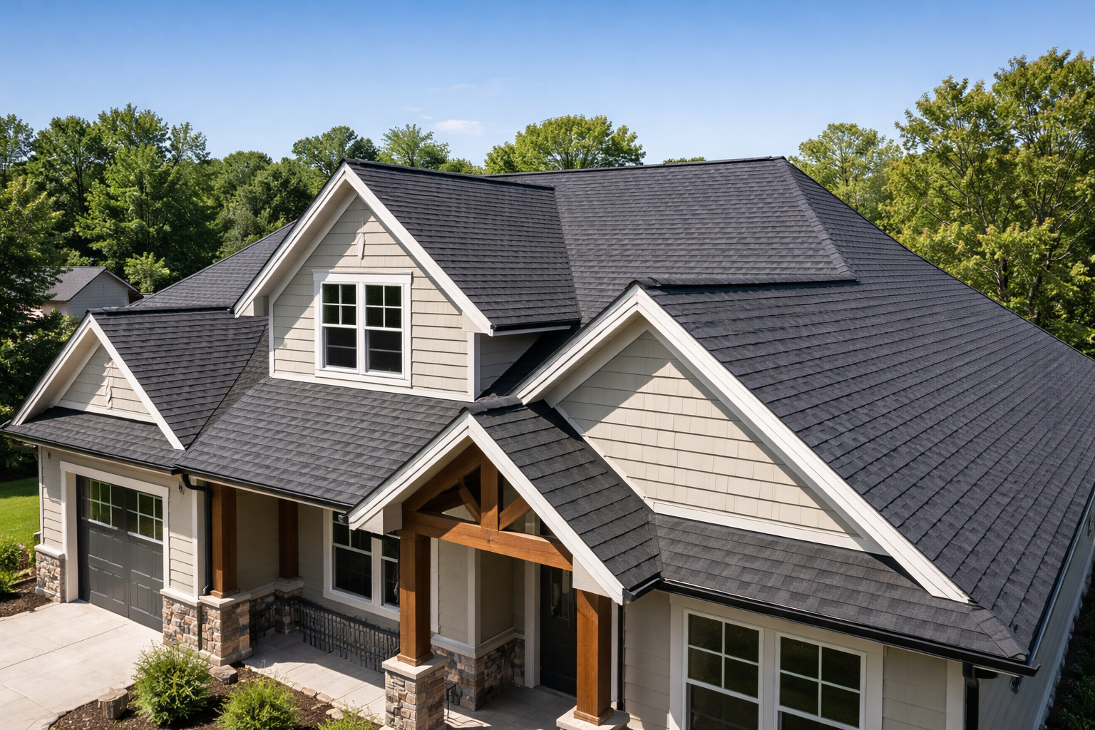 Une maison avec un toit en bardeaux noirs, un bardage beige et un porche en bois, dans un cadre boisé.