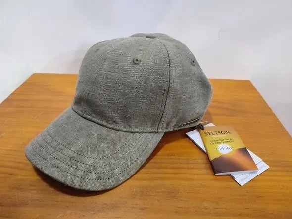 Una gorra de béisbol gris sobre una mesa de madera con una etiqueta de producto adjunta.