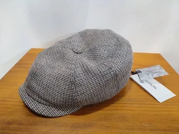 Gorra plana a cuadros grises con etiqueta, apoyada sobre una mesa de madera.