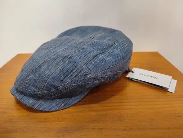 Gorra de tweed azul sobre una mesa de madera con una etiqueta blanca adjunta.