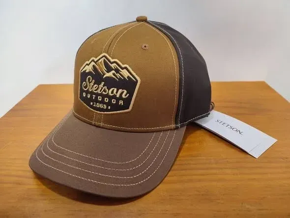 Gorra Stetson Outdoors de color marrón y beige con etiqueta, sobre una mesa de madera.