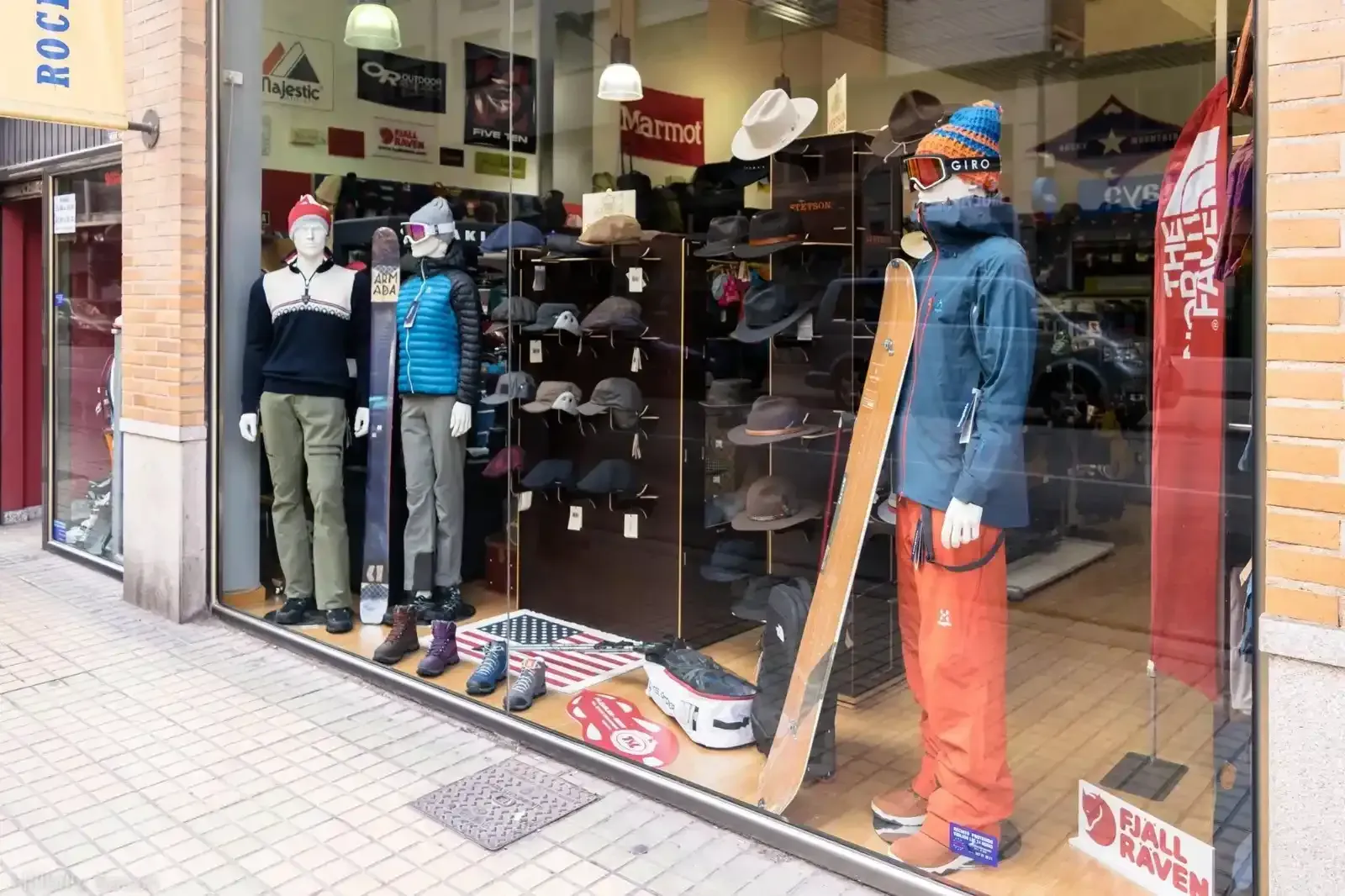 Escaparate de una tienda de ropa con maniquíes, sombreros, vaqueros y jerséis doblados en una acera de la ciudad.