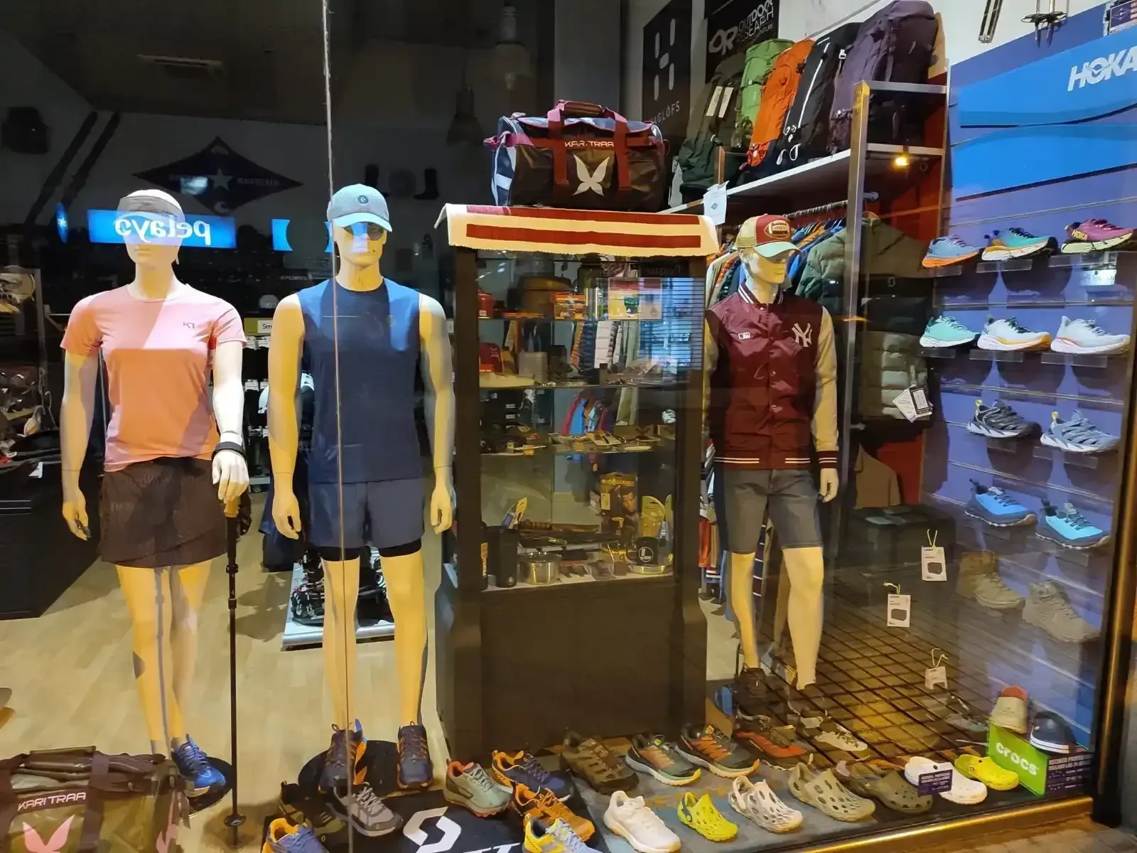 Exhibición en tienda de maniquíes de senderismo, zapatos y equipo para actividades al aire libre en una vitrina.