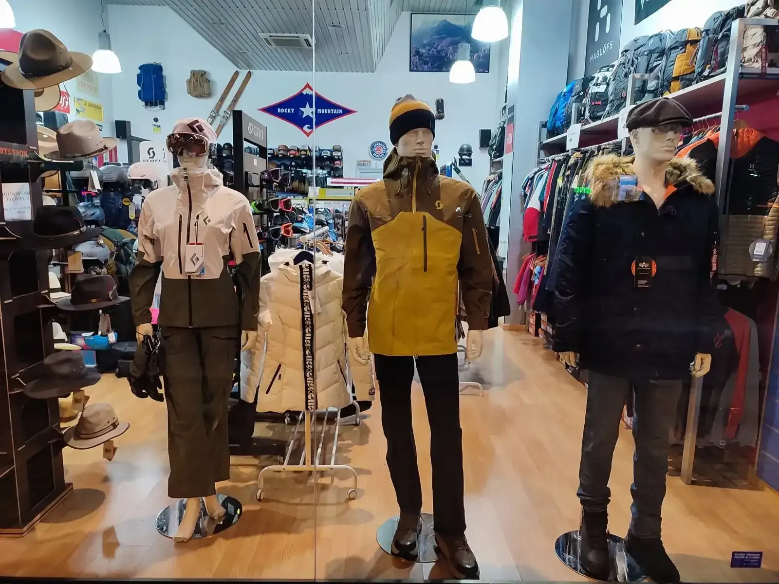 Maniquíes con chaquetas vintage en un pasillo de una tienda de ropa, junto a percheros con sombreros y conjuntos.