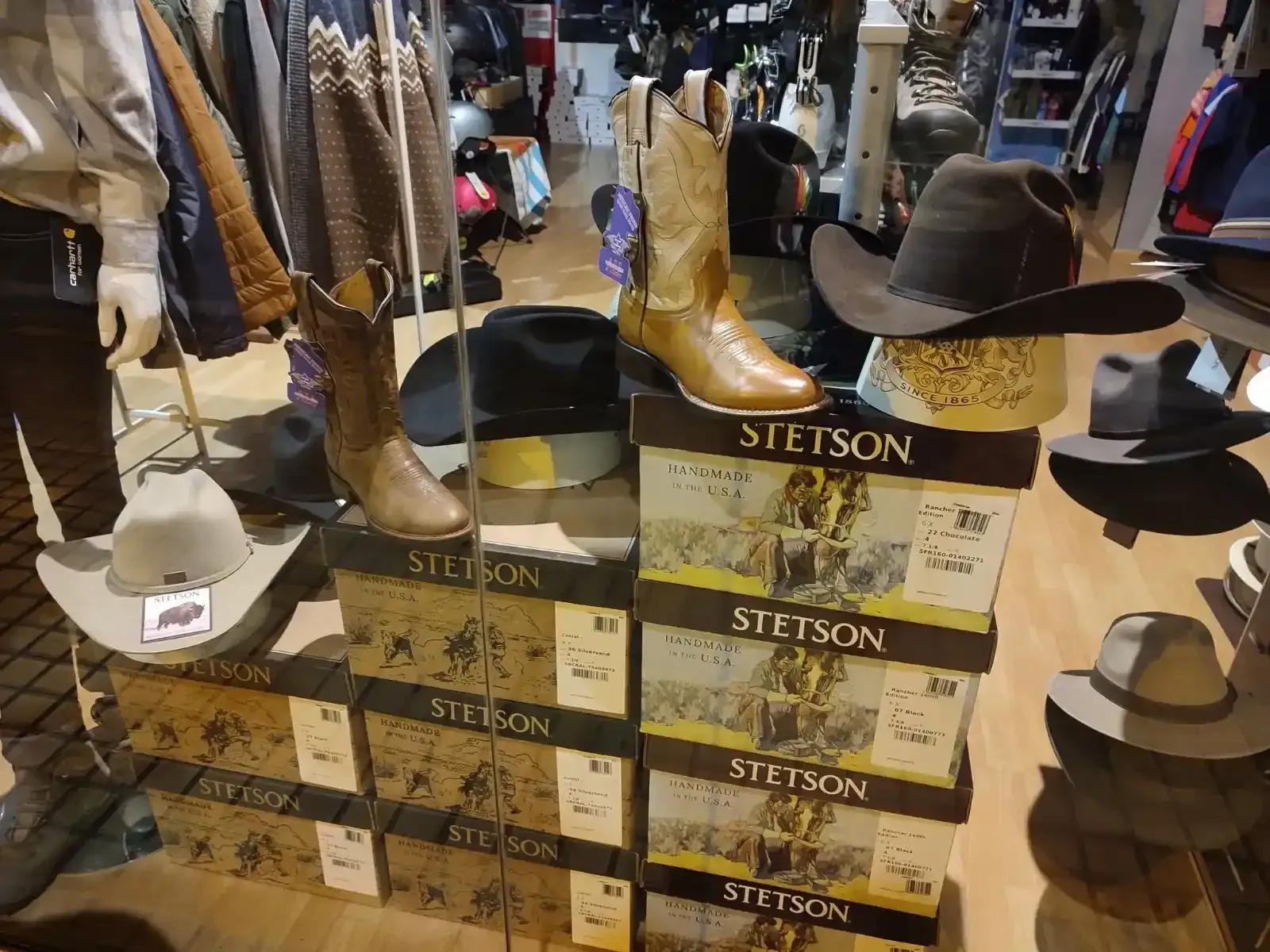 Botas y sombreros de vaquero expuestos en cajas Stetson apiladas en una tienda.