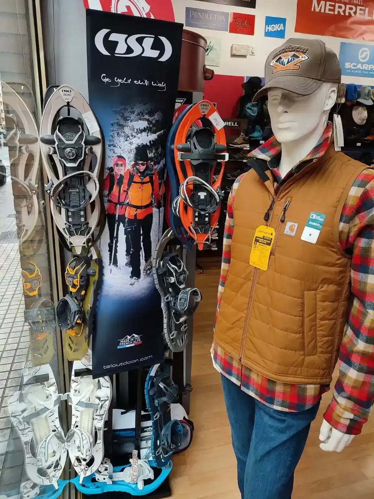 Raquetas de nieve y ropa de abrigo de invierno expuestas junto a un maniquí en una tienda.