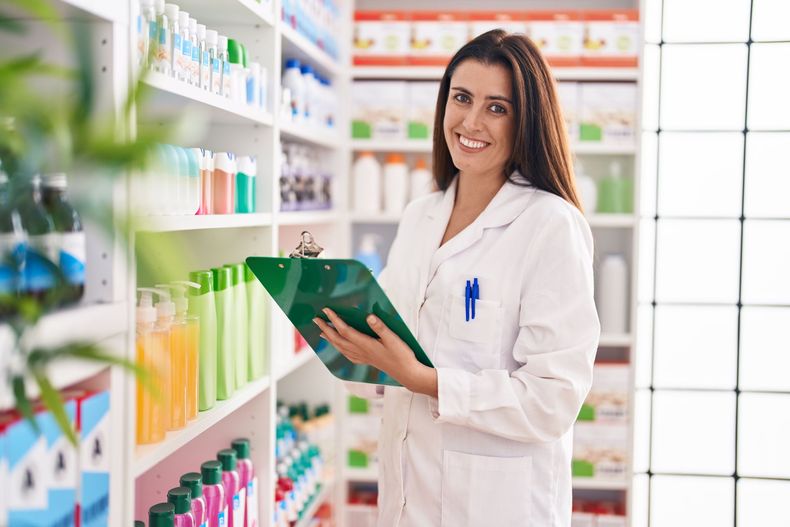Farmacista sorridente, con in mano un blocco per appunti, in una corsia della farmacia, circondato da scaffali pieni di prodotti.