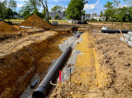 Chantier de construction avec de gros tuyaux noirs posés dans un sol boueux.