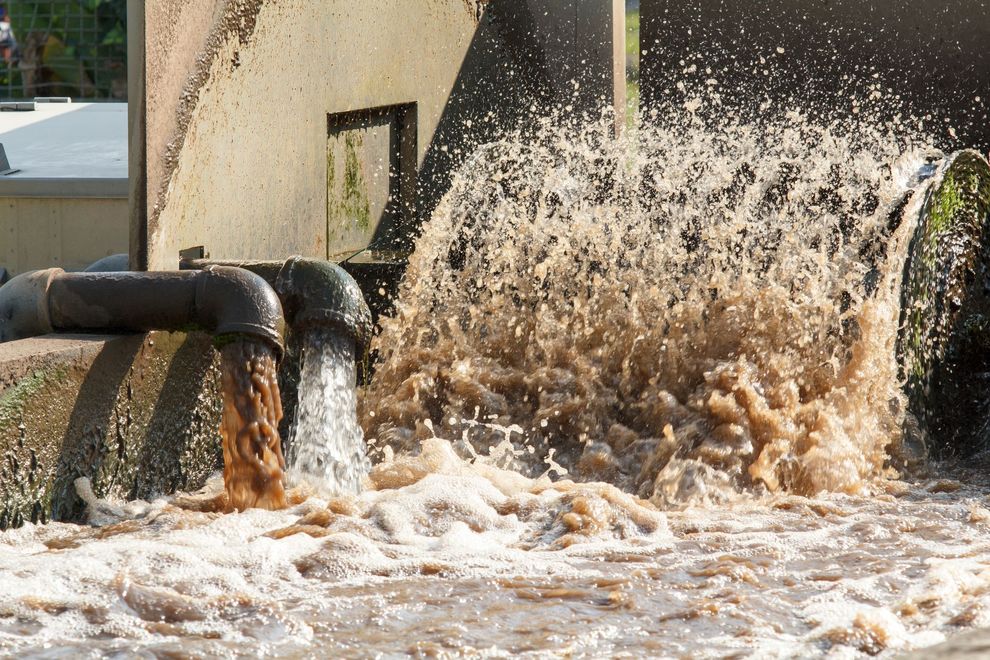 L'eau jaillit d'un tuyau noir dans un bassin ou un canal bouillonnant d'écume.